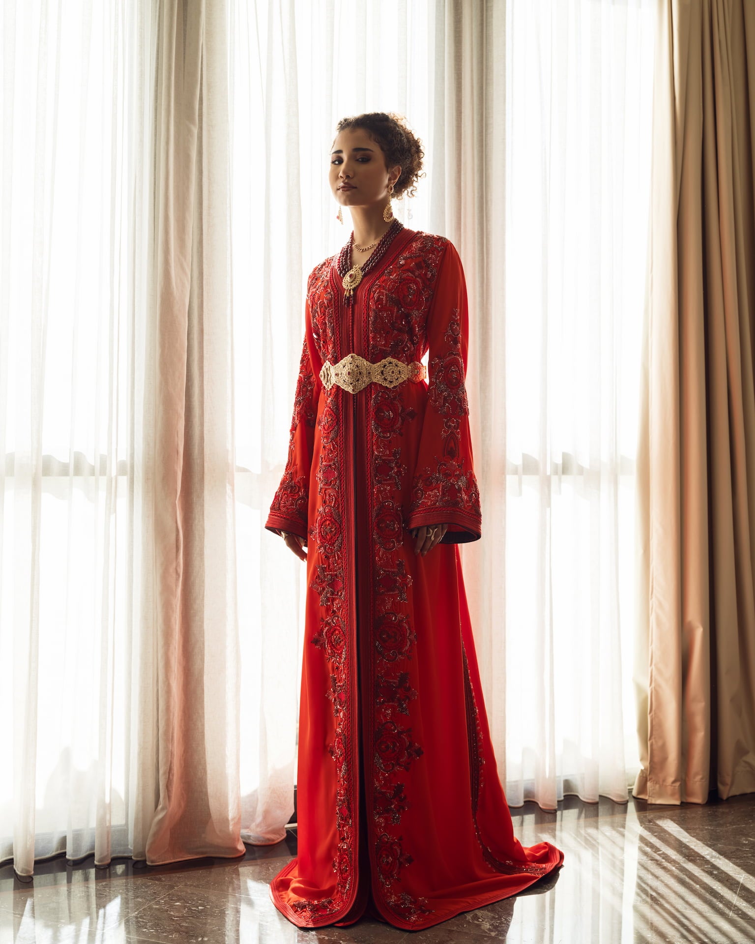 Deep ruby red Moroccan couture kaftan with elongated silhouette and gold embroidery, full-length view