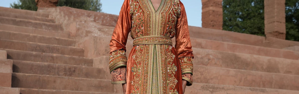Rust velvet Moroccan kaftan with gold and green embroidery against warm stone